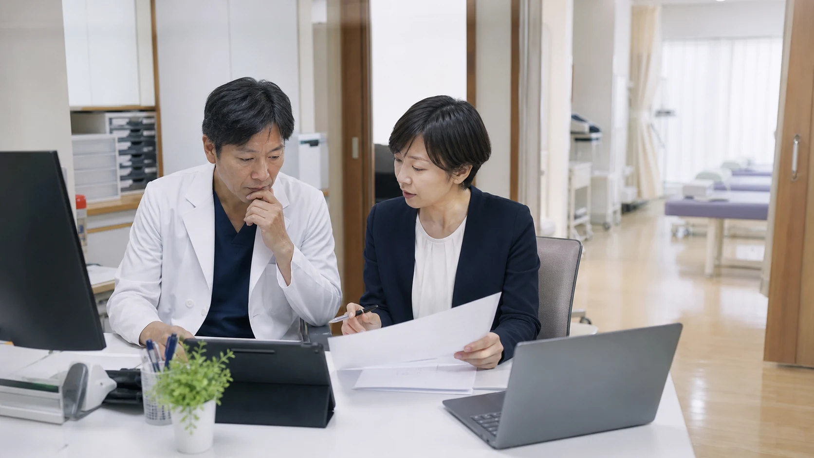 クリニックの院長・事務長・財務担当が診療報酬入金と医療機器更新を確認する場面